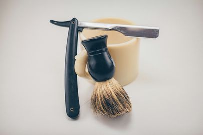 A straight razor and a shaving brush beside a pale ceramic bowl